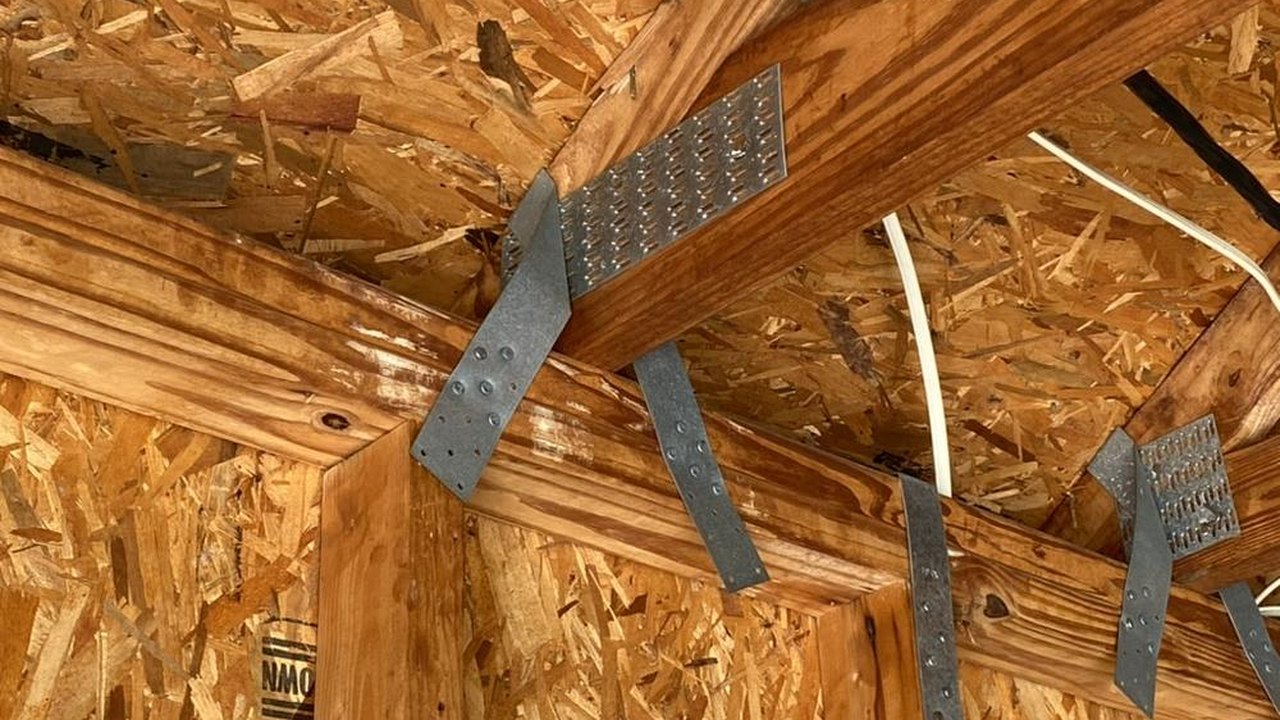 Metal hurricane clips and connector straps at the roof-to-wall connection inside an attic